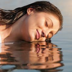 Smiling person with long hair rests face on water 
