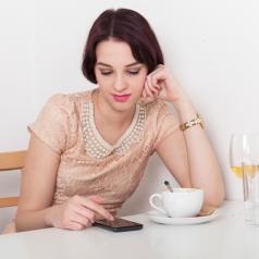 Person sitting in cafe looks at phone with bored or annoyed expression