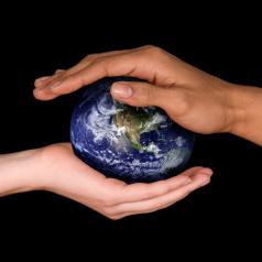 One hand each from two different people reach out and support small globe model of Earth on black background