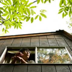 Photo taken from a low angle shows person looking out of large window on side of house