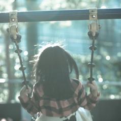 Blurred view photo of back of young girl sitting on swing