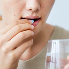 Close-up image of lower face of person taking a blue pill while holding a glass of water