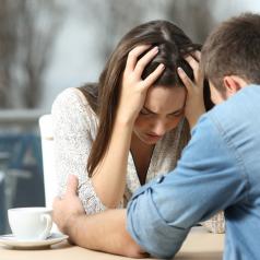 Two people sit at table in cafe, one upset, the other offering comfort and support