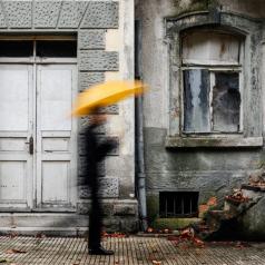 Blurred person holds umbrella outside broken-down house
