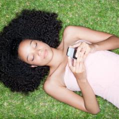 A teenage girl is lying on the grass with her phone.