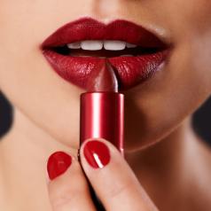A woman applies crimson lipstick.