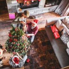 Overhead view of four people standing apart decorating Christmas tree