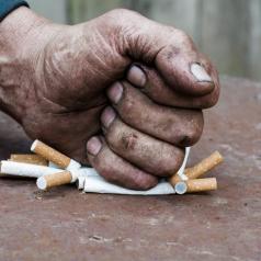 A fist crushes a pile of cigarettes.
