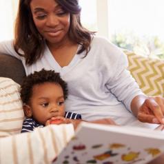 Parents read a book to their baby boy on the couch.