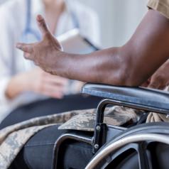 A veteran in a wheelchair speaks to a doctor in the background.