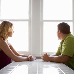 Two people sit at opposite sides of table, looking away from each other and out window