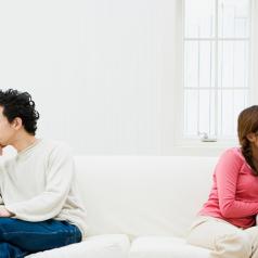 Two partners sit on opposite sides of sofa looking away from each other