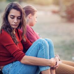 Two young adults sit on bench, space between them, looking away from each other