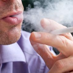 A closeup of a man breathing out cigarette smoke