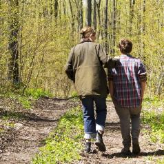 Rear view of parent and youth walking on trail in woods and talking