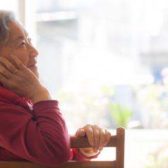 Senior adult with short hair sits at table, face resting on hand, looking into distance thoughtfully