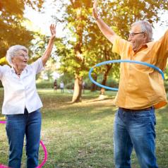 Active senior couple plays hula hoop together in park