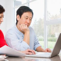 Adult couple sits at table working out finance plan with computer