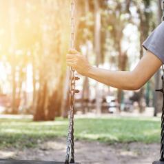 Arm of person who is sitting on swing alone reaches to hold chain of other swing