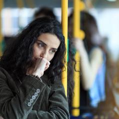Person with long, curly dark hair holds hand to mouth thoughtfully while riding train home