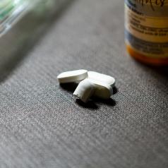 A photo of white pills on the floor next to a prescription bottle and a ziplock bag.