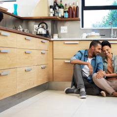 Couple looking happy together sit on kitchen floor talking together and smiling