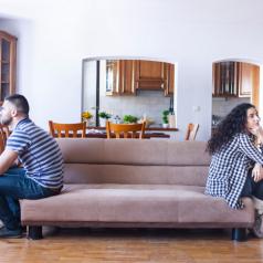 Partners sit on opposite ends of sofa, turned in opposite directions and facing away from each other