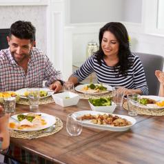 Two parents and two children sit down at the table to enjoy a meal together, talking and smiling
