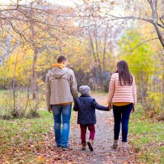 Rear view photo of two parents and child walking along path in park in autumn