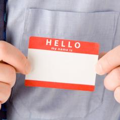 A close up of hands attaching a blank name tag next to a blue tie.