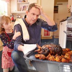 A man pulls a burnt turkey out of the oven. His daughter watches from behind his back.