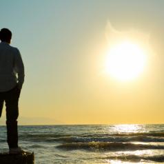 A man stands with his hands in his pockets, overlooking the ocean waves.