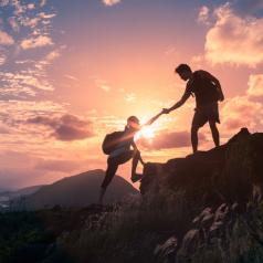 Hikers help each other up mountain under setting sun
