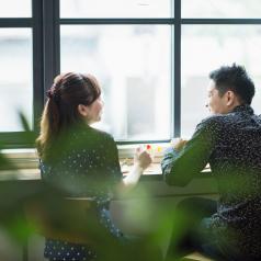 Adult couple sit at window table in cafe, facing each other and talking