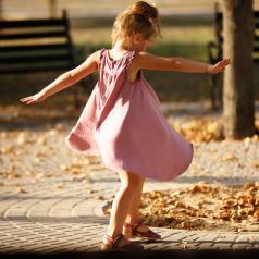 Child in pink dress dances outside among autumn leaves