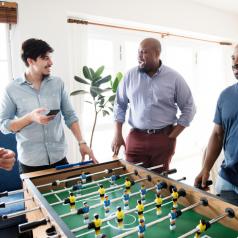 A group of men in button up shirts stand around a foosball table.