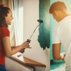 Couple working together talking and laughing while painting a room