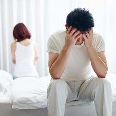 A couple, both who have faces down or turned away, sit on opposite ends of bed