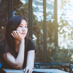 Woman sits at table in outside cafe, looking thoughtful