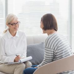 Therapist sits on couch across from person in therapy, smiling and talking.