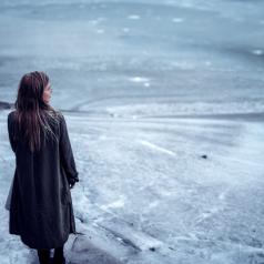 A woman stands alone on a frozen lake.