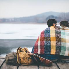 Couple wrapped in blanket sits looking out over lake