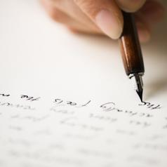 Close-up of a hand writing a letter with an old-fashioned pen.