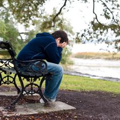 Child in jeans and hoodie sits on bench with head in hands