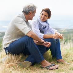 Mature adult couple sit on rock talking openly and smiling