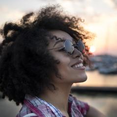 Young adult with natural hair smiles and looks up outside at sunset