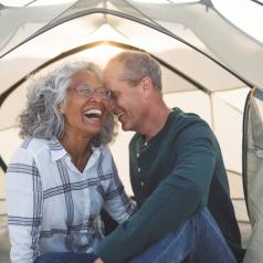 A man whispers to his laughing wife inside a cozy tent.