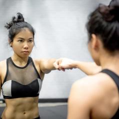 A woman in gym clothes touches her fist to her reflection.