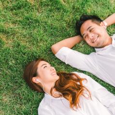 A young couple wearing white shirts lie side by side on spring grass.