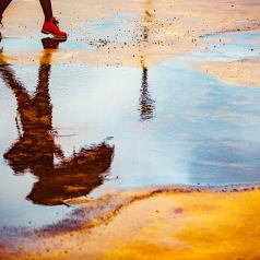 Reflection of woman walking with an umbrella in a puddle